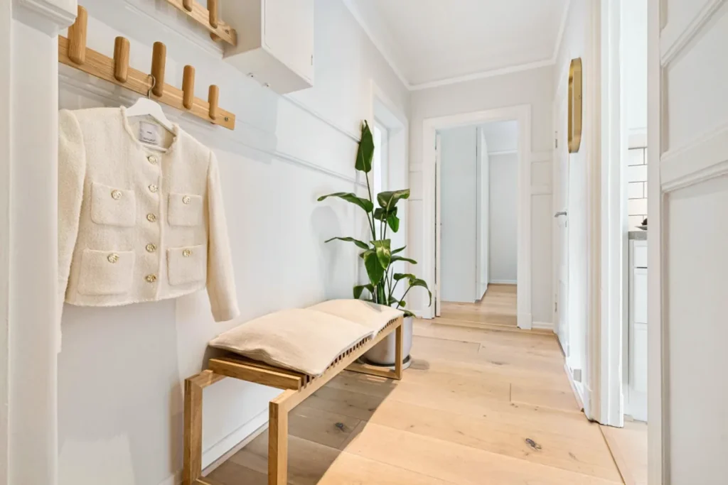 Organized entryway with wooden bench, coat hooks, and plant