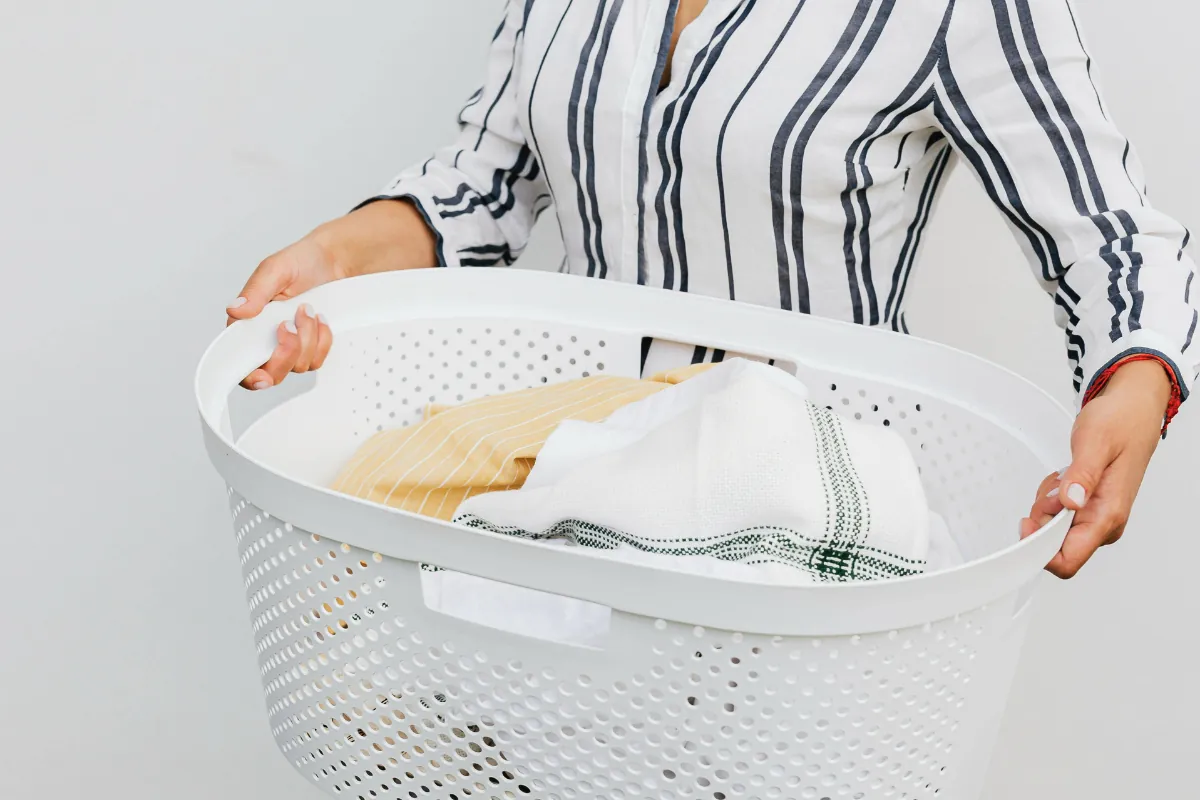 Person holding a white laundry basket with clean folded clothes