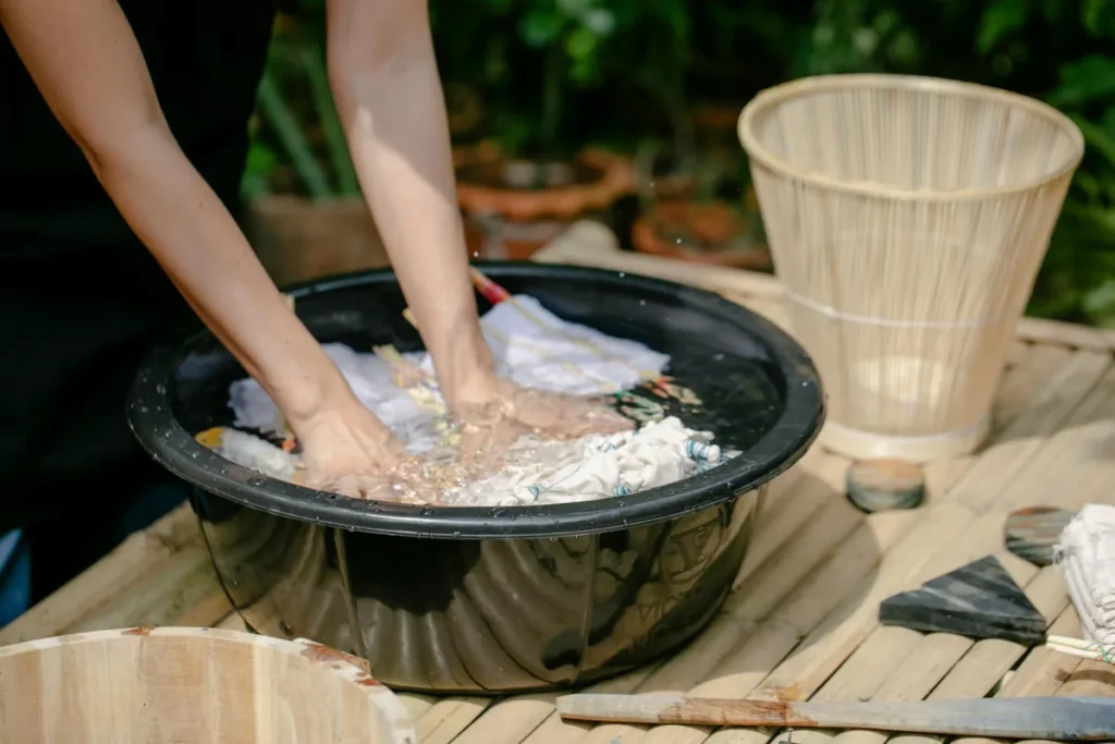 Hands soaking stained clothes in a wash tub outdoors