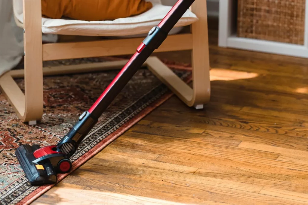 Cordless vacuum cleaning a rug beside a hardwood floor