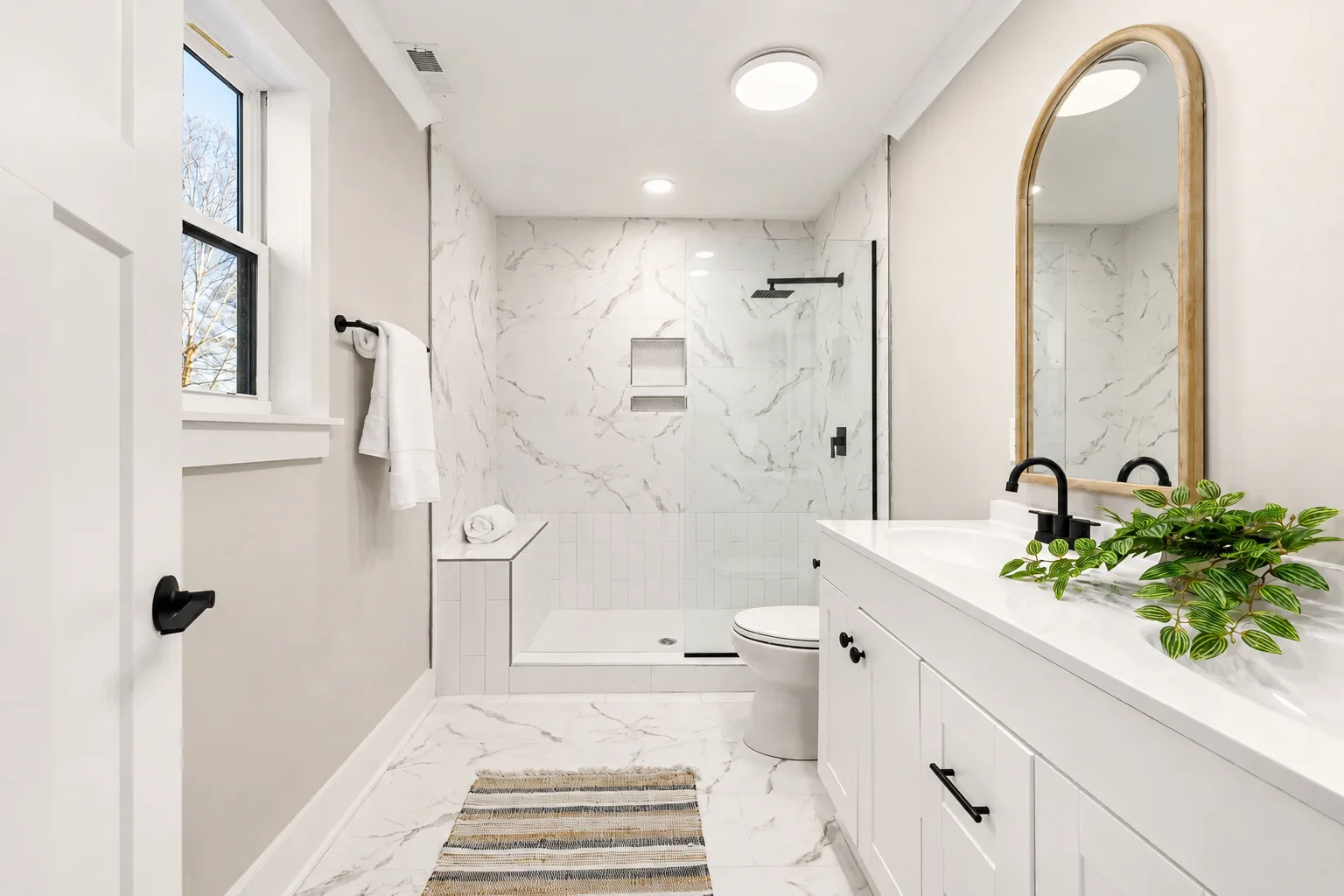 bright modern bathroom with glass shower, white vanity, toilet, and marble tile